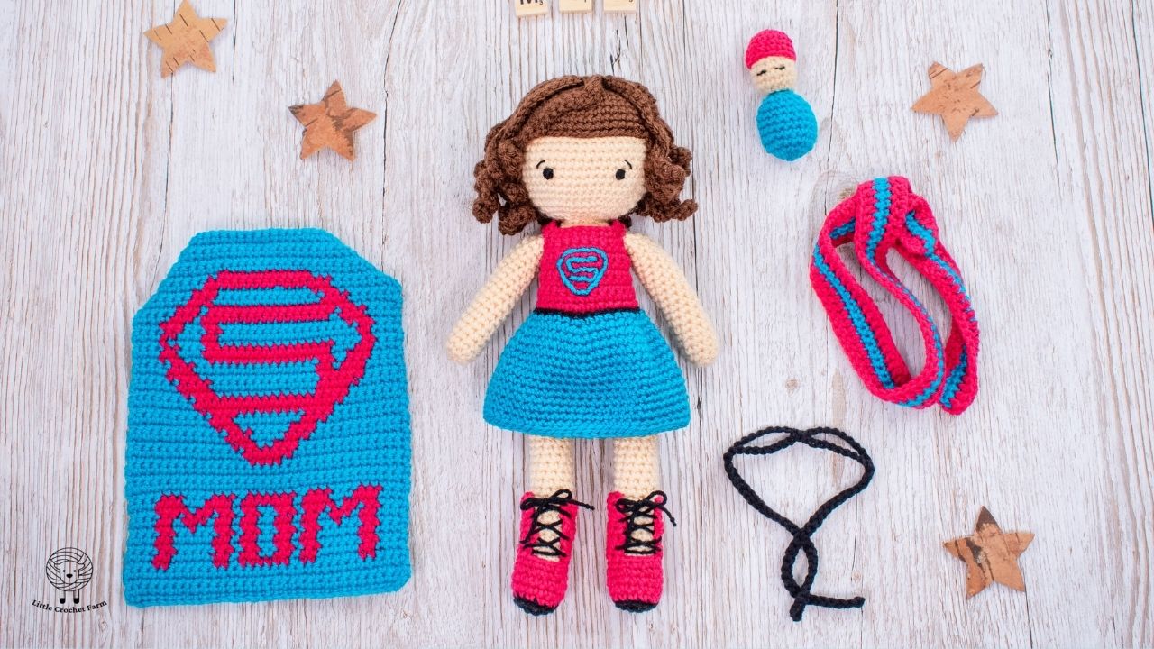 a crochet super mom doll free pattern with removable cape, mask, accessories and a baby on top of a wooden table